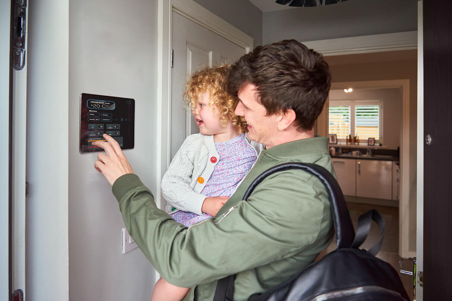 Mann mit Kind auf dem Arm im Haus, der ein Touchpanel an der Wand bedient