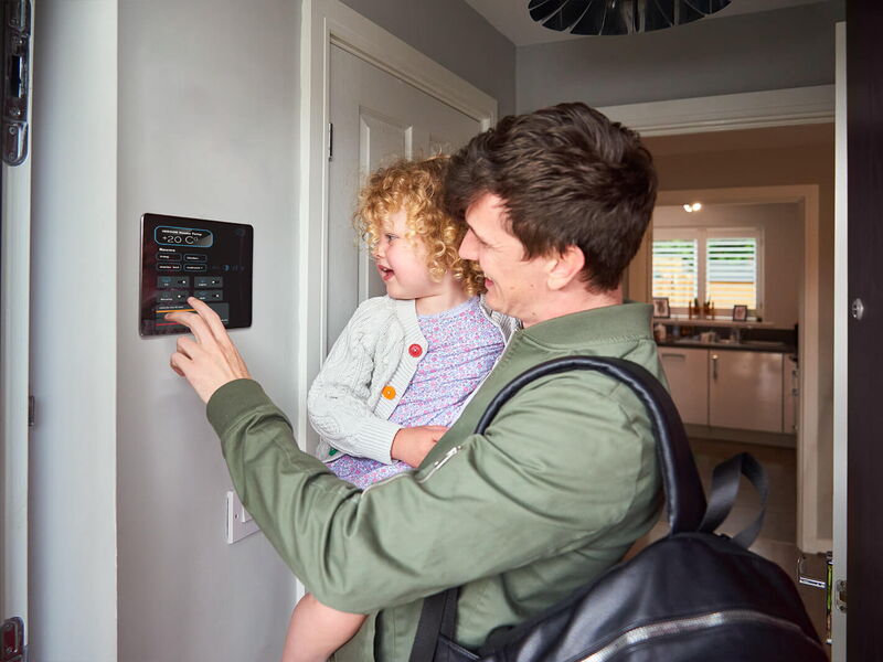 Mann mit Kind auf dem Arm im Haus, der ein Touchpanel an der Wand bedient